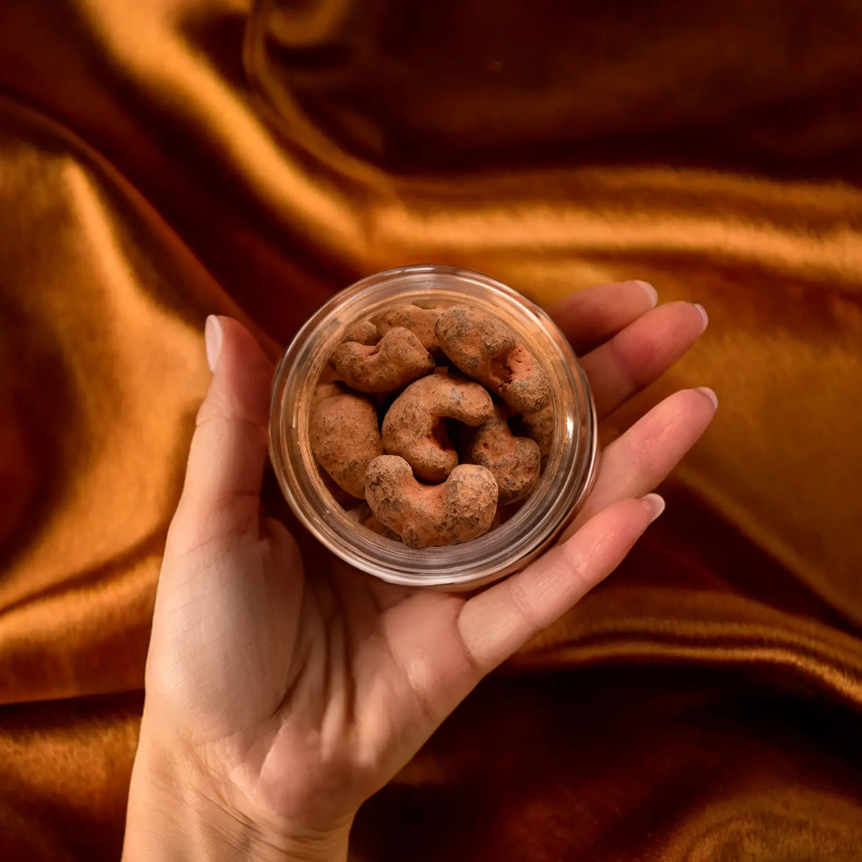 Hand holding an open small 50g glass jar of 75% dark chocolate roasted cashews 